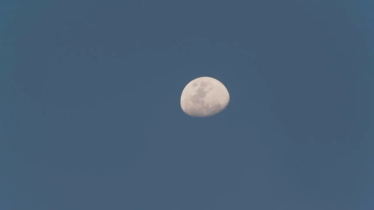 Close up of the moon moving slowly captured during the day with a clear blue sky in 4K