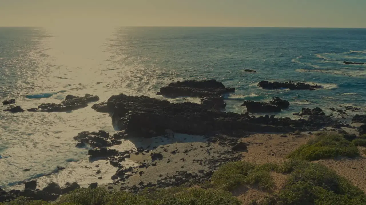 the sun reflects brightly on the Pacific ocean as the waves roll onto the rocky shore at Kaena Point Oahu Hawaii