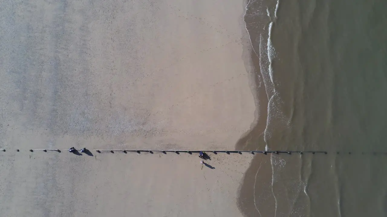 Sunny aerial view looking down over golden sandy beach and dividing ocean waves with tourists