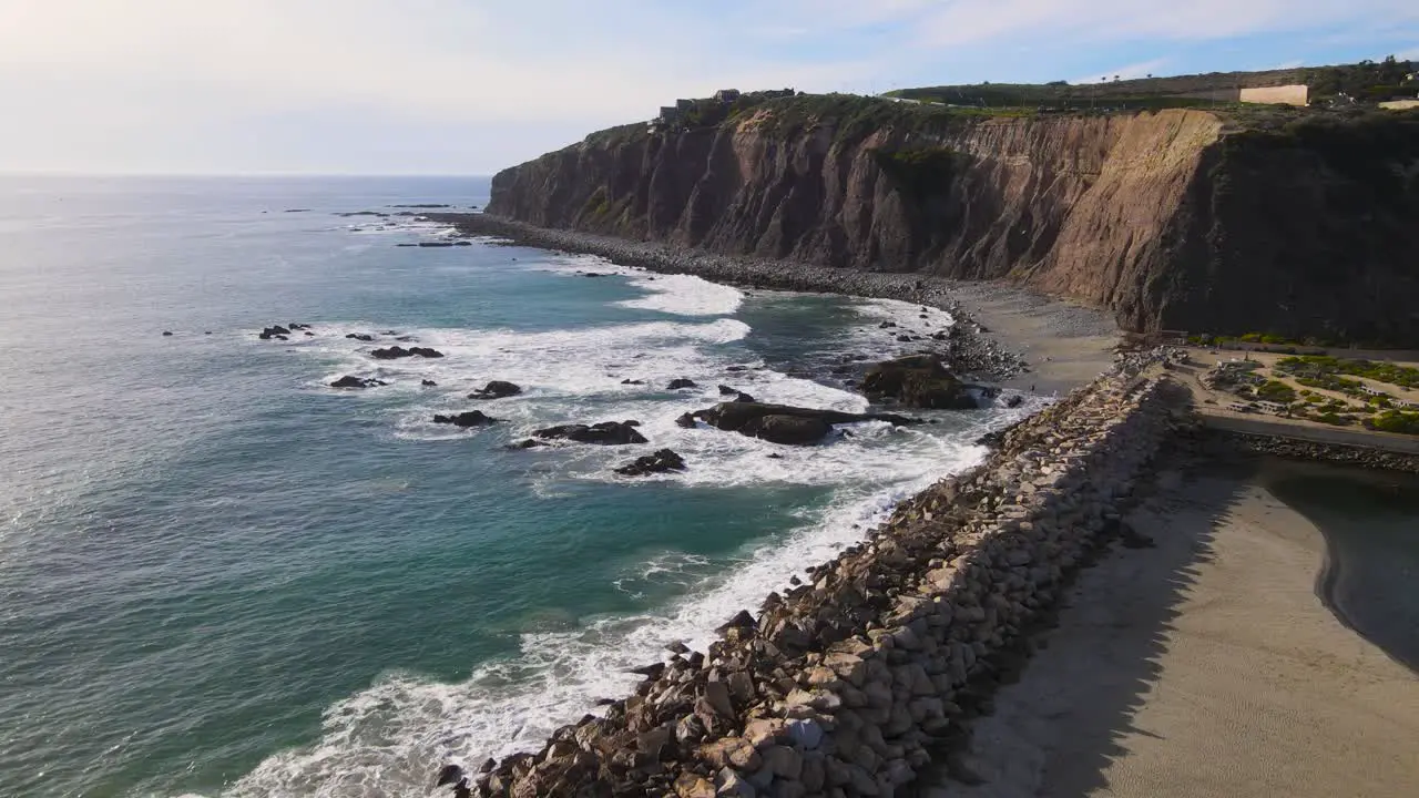 Aerial dolly over rock wall ocean waves crash in front of majestic sea cliff