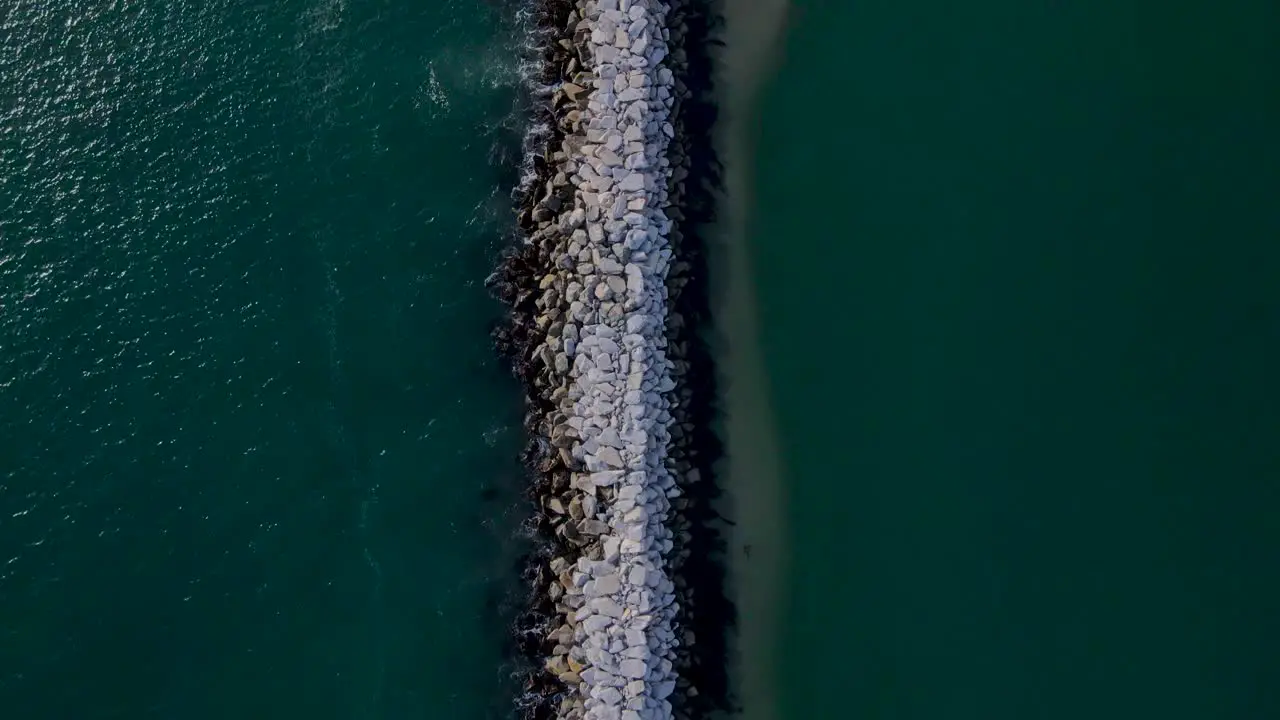 Birdseye view of rock wall ocean jetty creating a sand bank sunny day