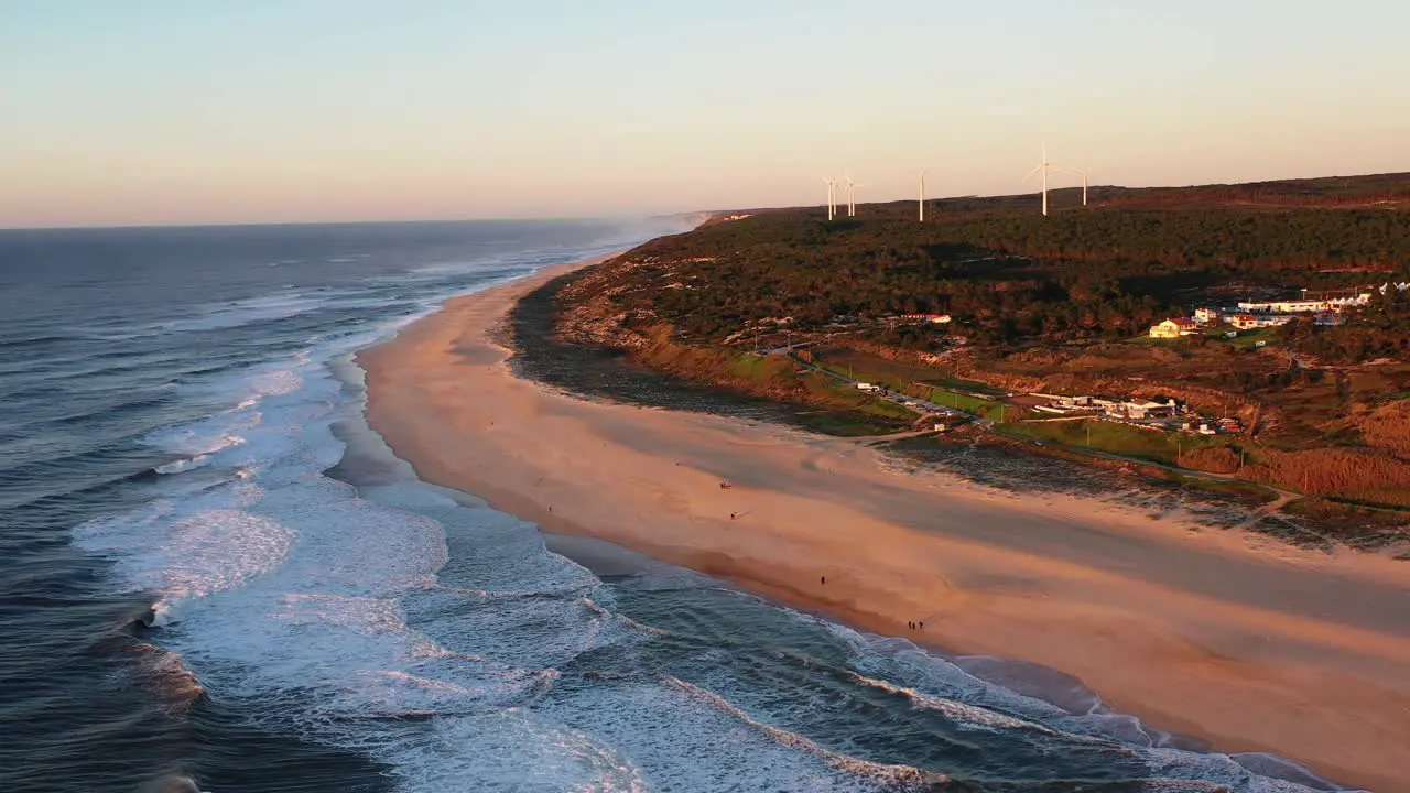 Praia do Norte Beach in Nazare Portugal with string waves and wind turbines in the distance Aerial pan left shot