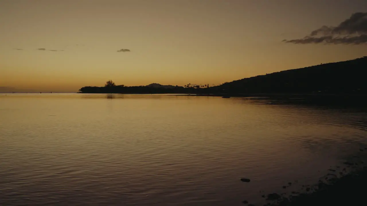 stationary shot of the volcanic mountains of Oahu Hawaii are a silhouette against the orange sky as it reflects on the calm waters of the Pacific ocean just after sunset alpenglow