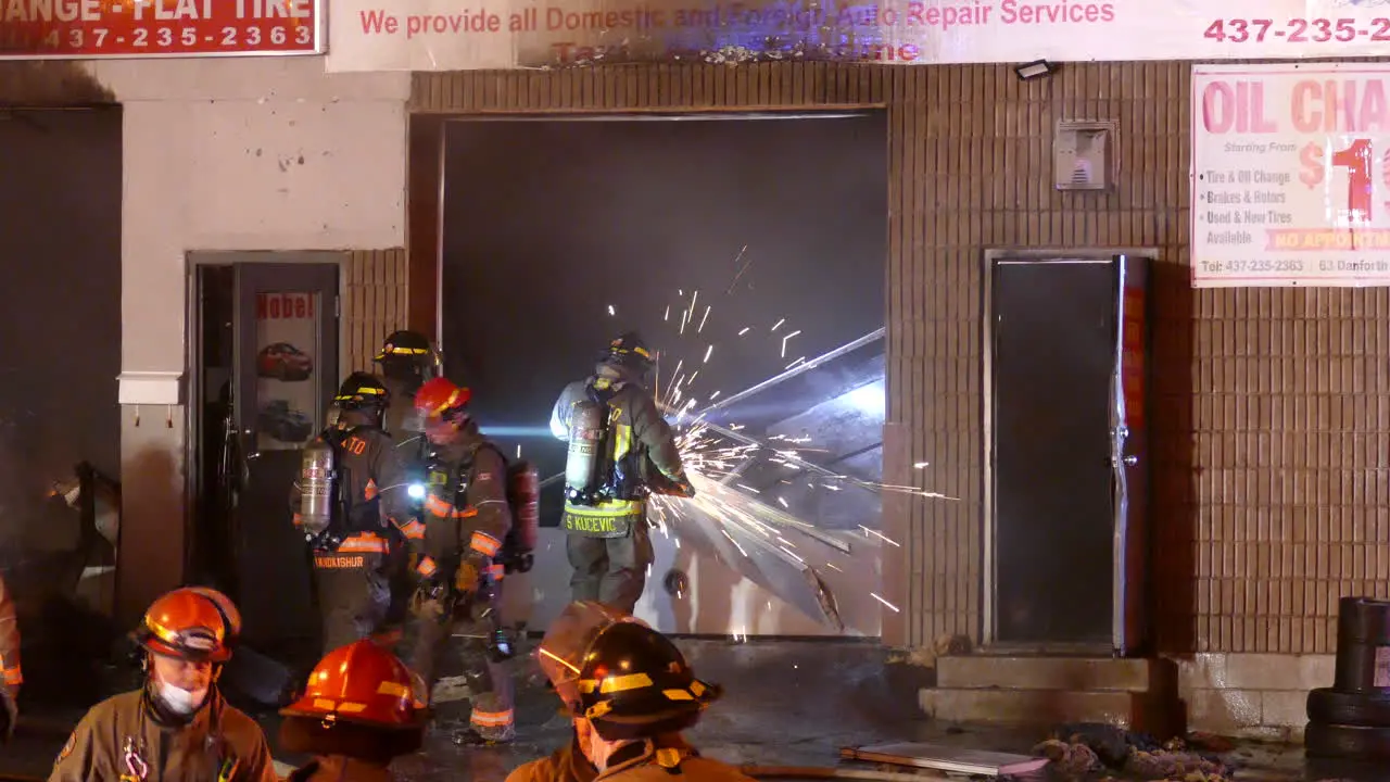 Firefighter Crew Using Circular Saw Cutting through Garage Doors of 'Danforth and Warden' Auto Body Repair Shop in Scarborough Toronto