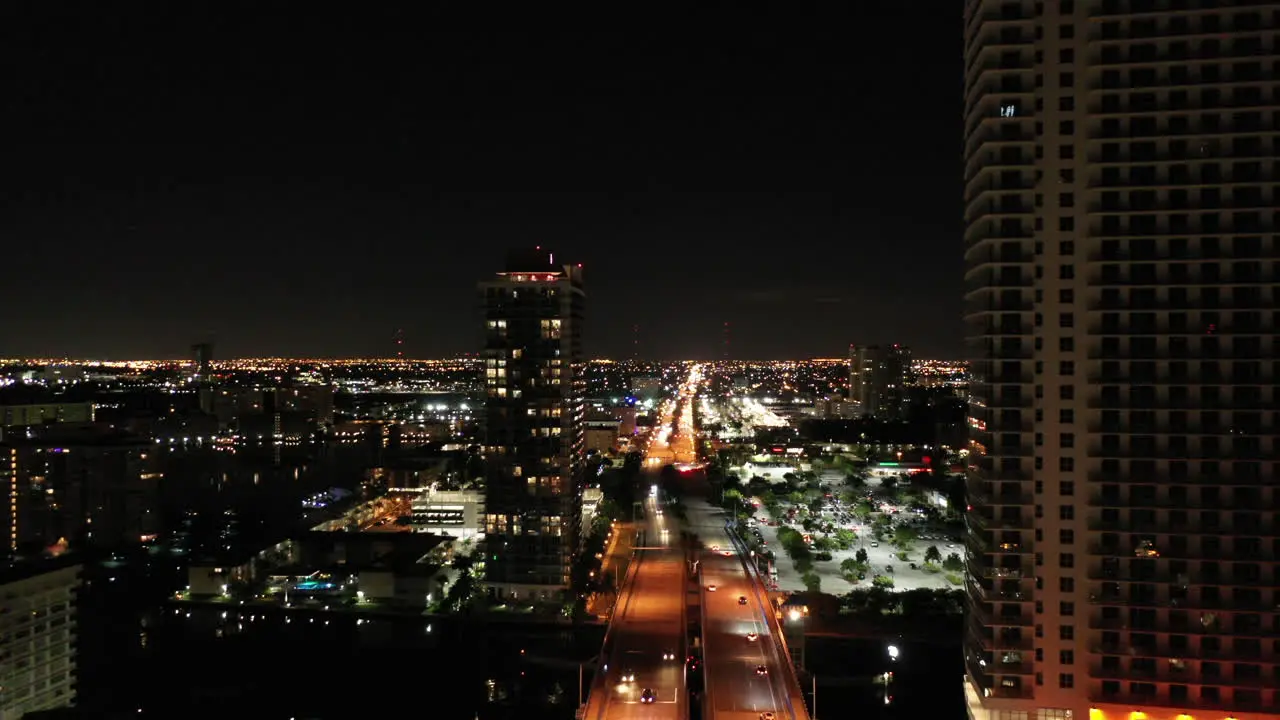 Aerial night time dolly through buildings over streets in Miami