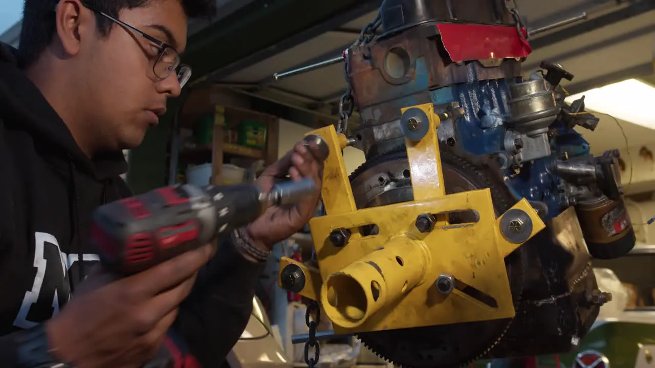 Young mechanic unscrewing screws with a drill from engine stand