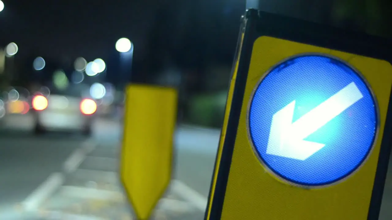 Night time road traffic sign pointing direction with traffic bokeh as traffic passes by