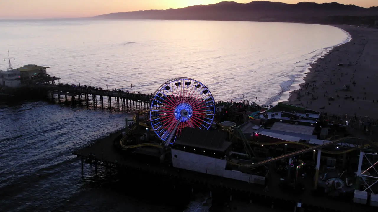 Dusk sunset drone shot pulling back from lit up santa monica pier