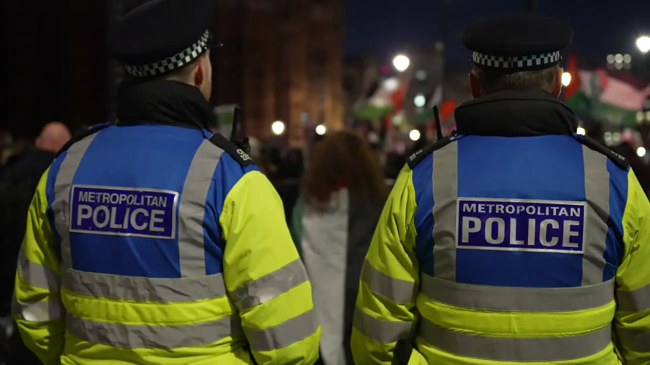 In slow motion two Metropolitan public order intelligence police officers stand watching and monitoring a nighttime protest outside Westminster Abbey