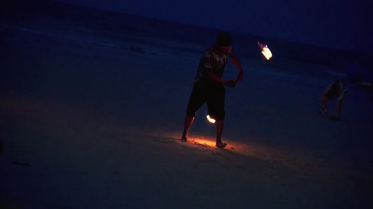 Performer spinning two flaming torches at night at beach fire show