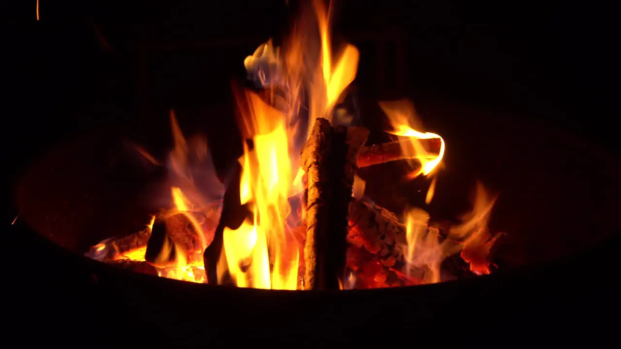 Campfire flames burn firewood bright orange during night at outdoor campsite