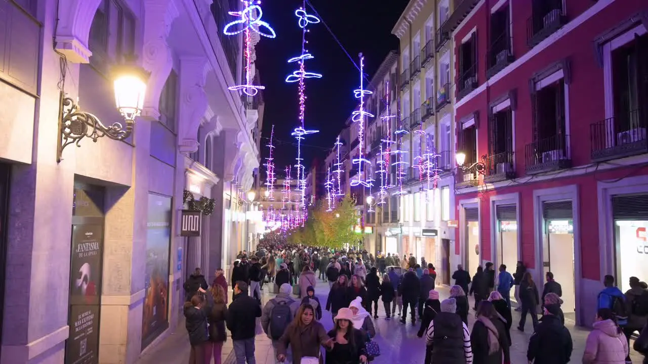 People walk through a crowded pedestrian street illuminated with Christmas purple lights during the Christmas holiday