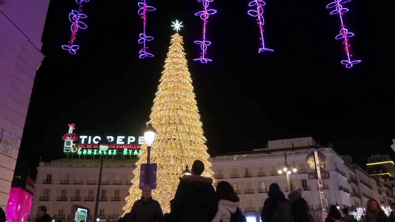 People are seen enjoying an illuminated Christmas tree installation decorated with gold LED lights during the Christmas holiday at Puerta del Sol Square in Madrid