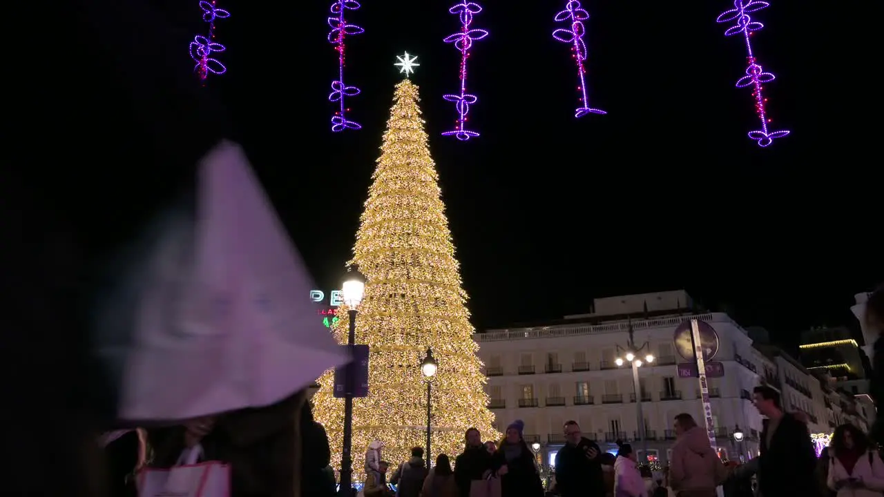 People walk past an illuminated Christmas tree installation decorated with gold LED lights for the Christmas festivities and holiday at Puerta del Sol square in Madrid