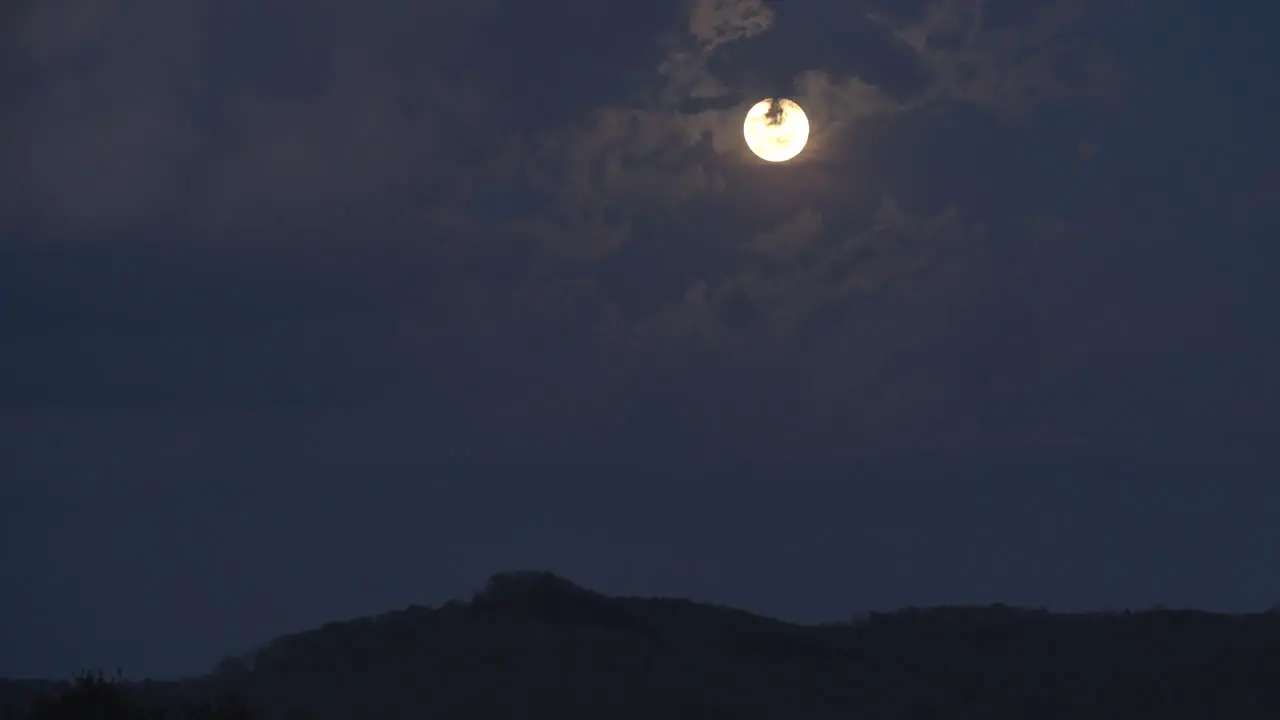 A spring time day to night timelapse of a moon rise behind puffy clouds in the Appalachian hills