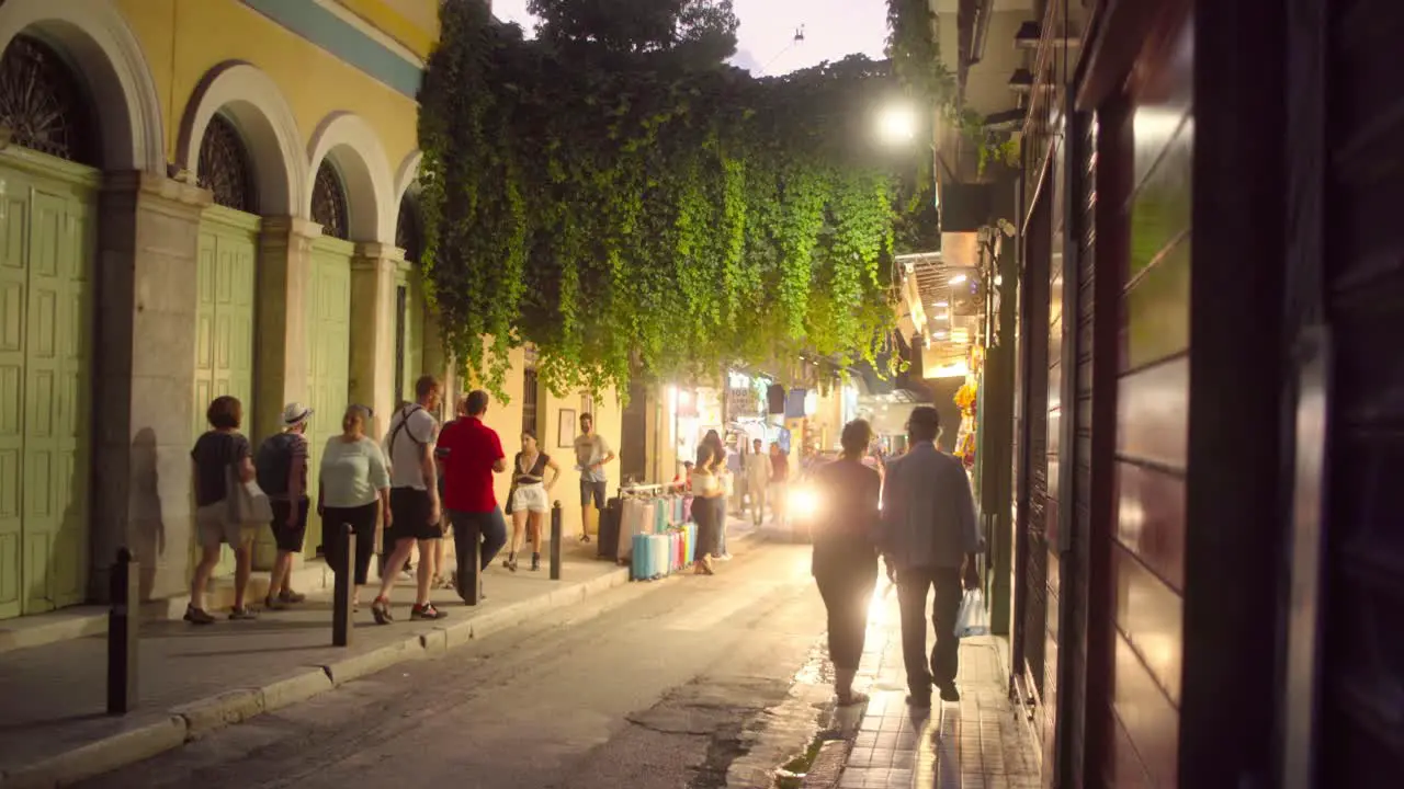 People walking down a narrow street in Athens backlit by a cars headlights