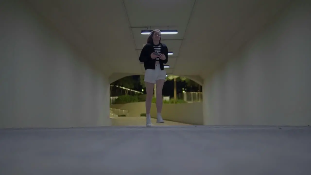 A girl with medium-length blonde hair runs through a luminous tunnel in a skateboard park with her hair waving freely as she runs -- shot at a low angle