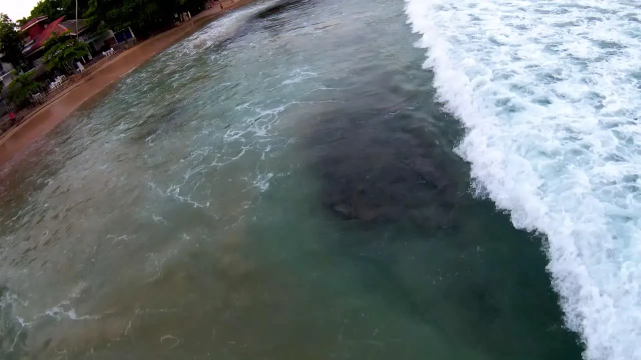 Aerial dolly in lowering on turquoise sea waves hitting sand shore near tropical vegetation in Mirissa beach Sri Lanka