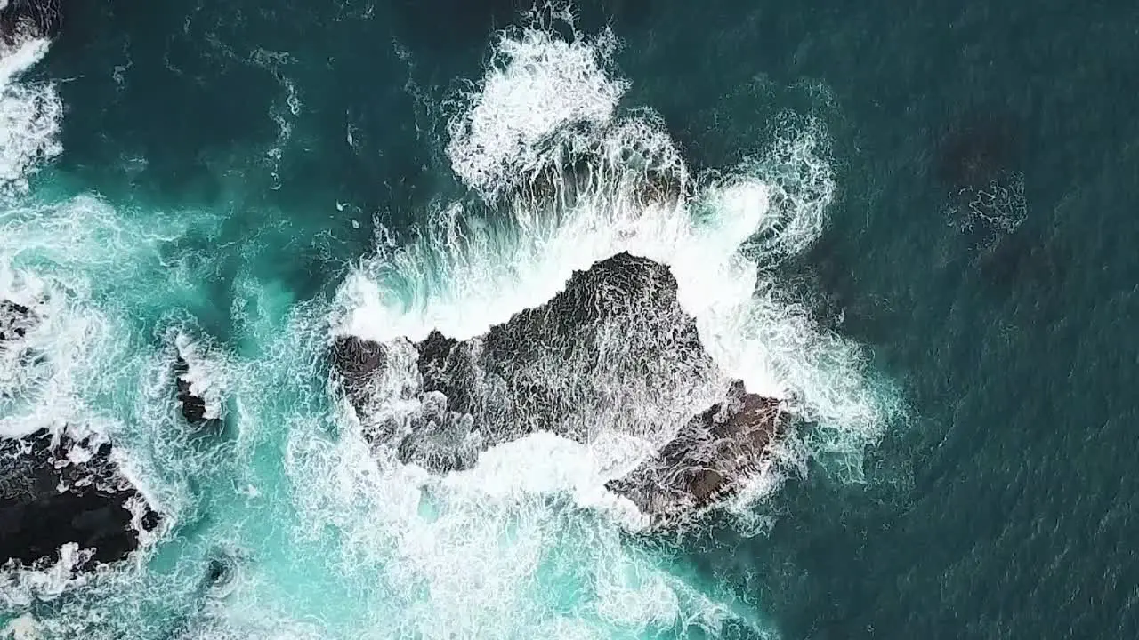 Slow motion aerial of waves surging over rock shelf in deep aqua blue ocean