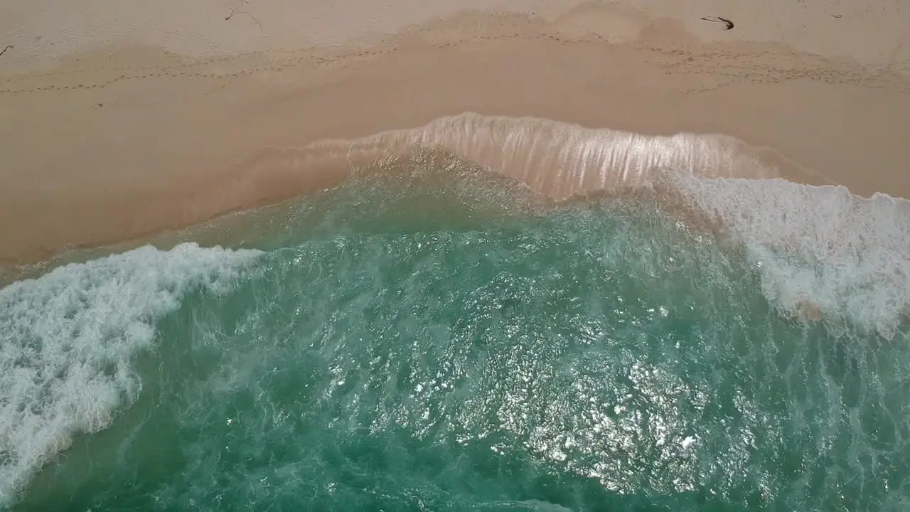 Blue waves crashing into a prestine beach top down view from a drone