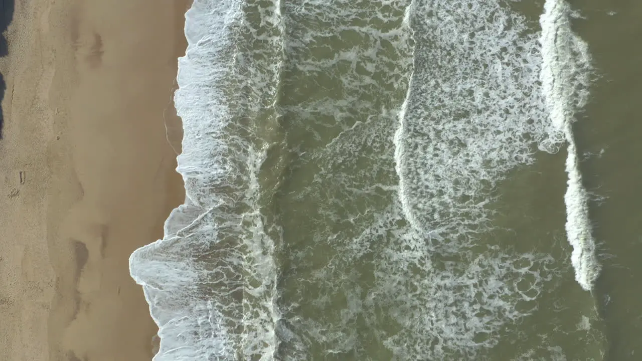 Slow aerial shot of a deserted golden sand beach and powerful white foam waves crashing