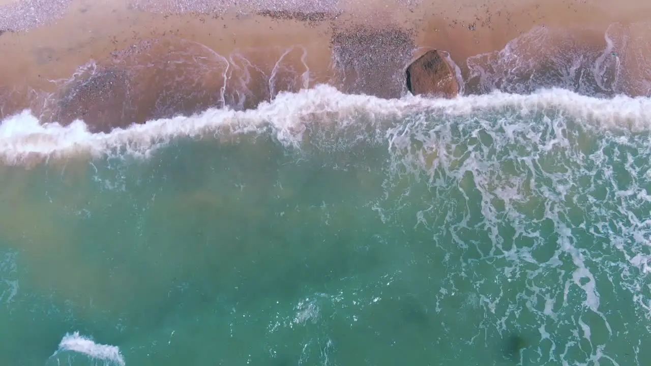 Top down aerial view of tropical beach with waves crashing against shore