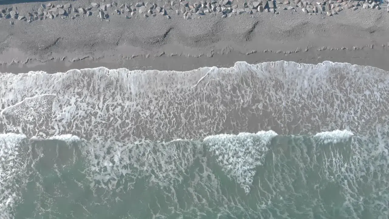 Descending birds-eye perspective of ocean waves crashing on the sand then retreating