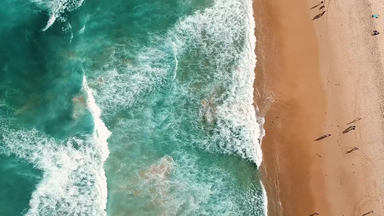 Top down birds of view of a beautiful tropical beach with waves crashing into the sandy shore with many people walking