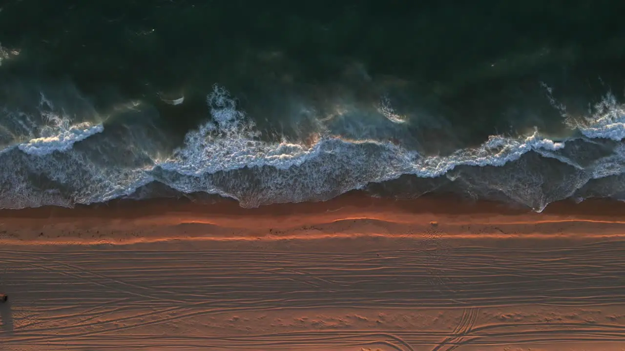 A stationary birdseye view shot of the shoreline with strong waves of water during the golden hour