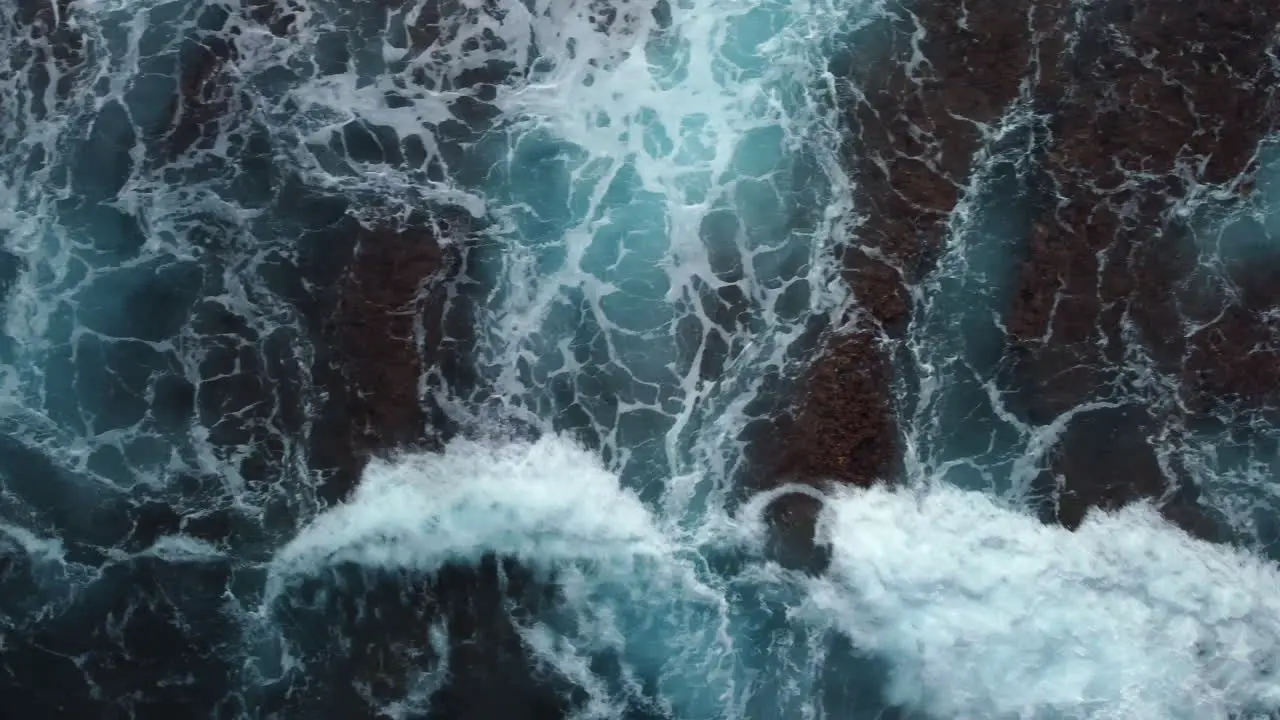 Bird's eye view of powerful waves crashing on rocky coastline tracking shot