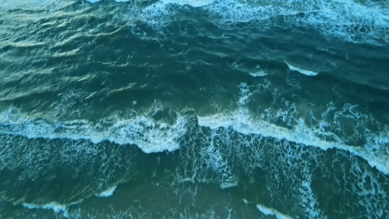 Aerial tilt up shot of stormy day with breaking waves at ocean shore with sandy beach