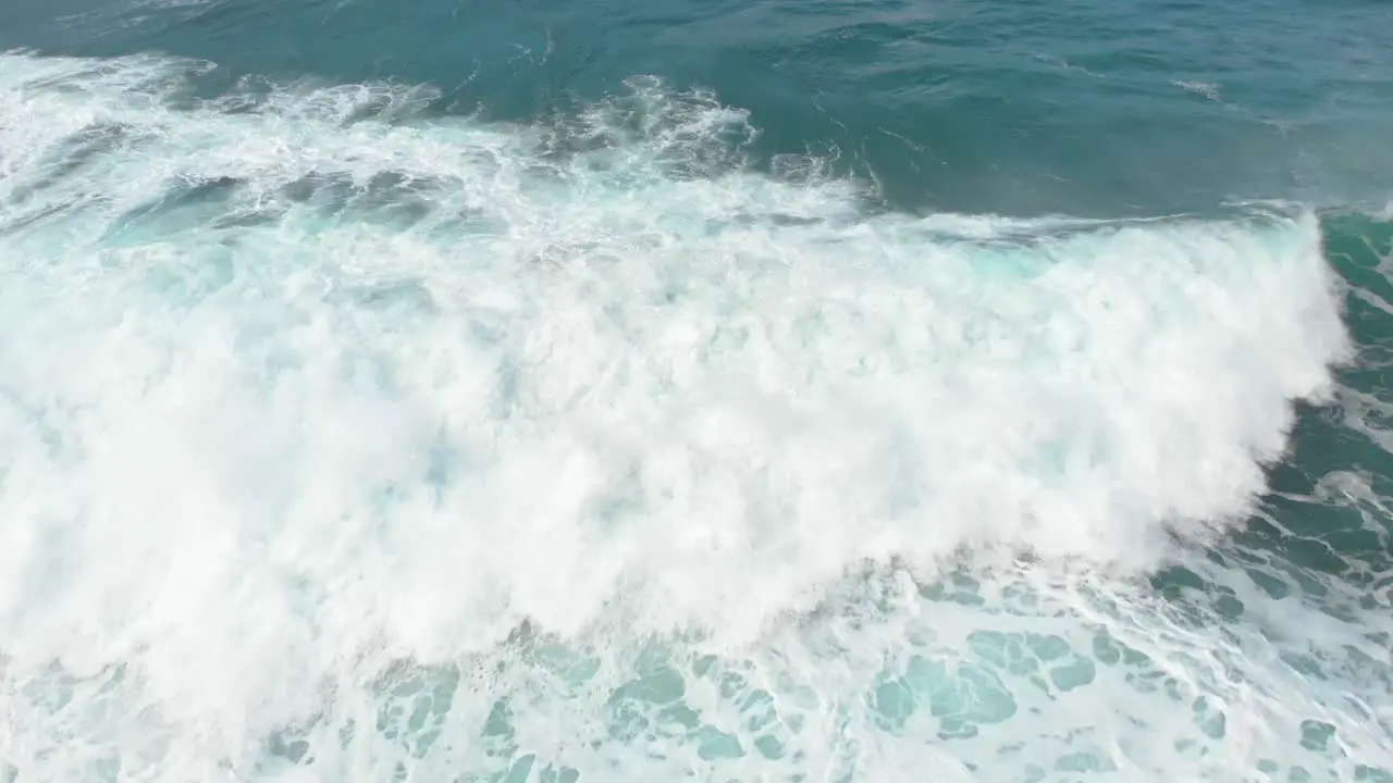 An interesting aerial birds eye view shot following a wave crashing into shore as the white wash swirls around the water