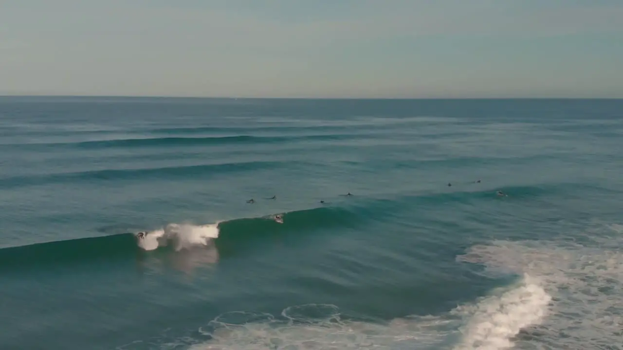 Aerial Shot Of People Surfing In Sea During Sunset Drone Flying Backward Over Ocean