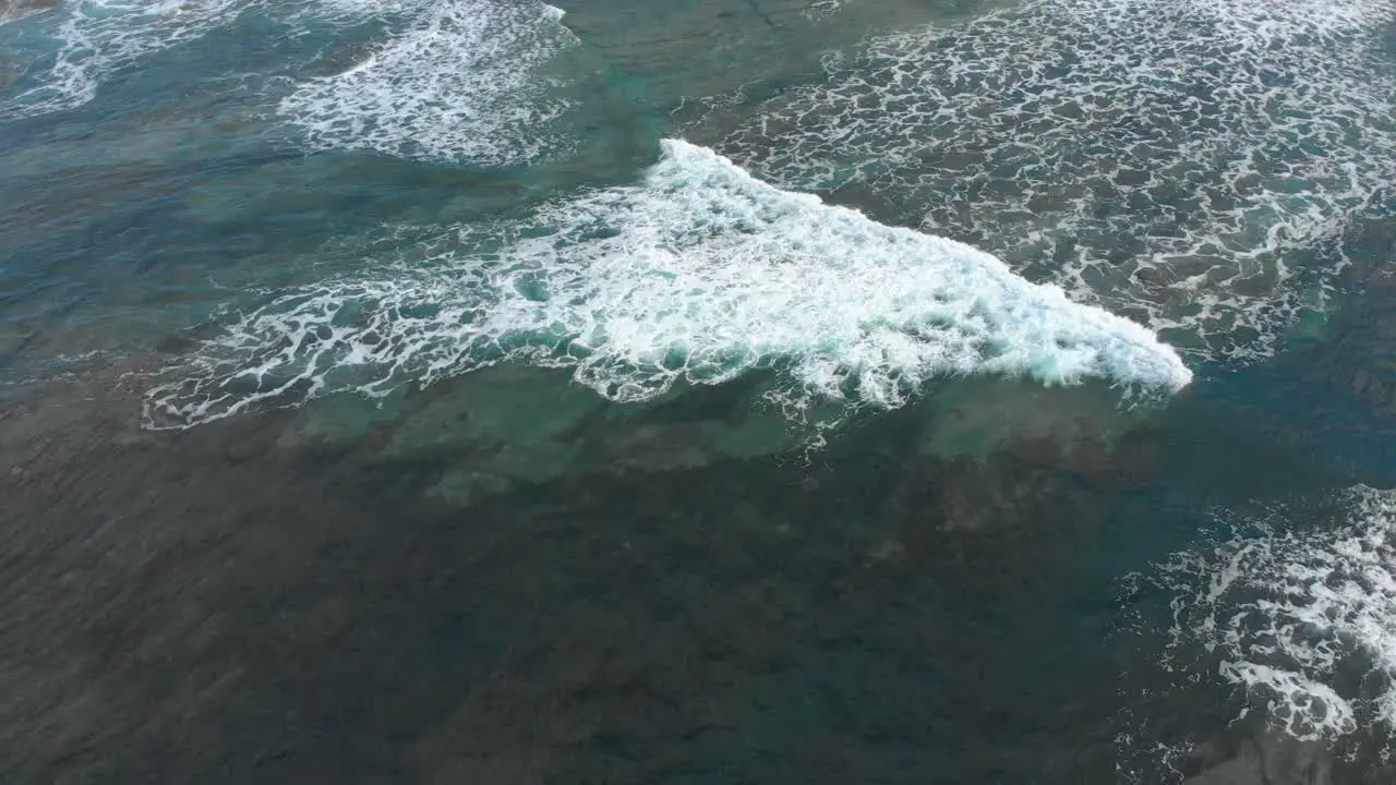 A birds eye aerial orbit shot of a waves white wash washing across a reef in blue water off Australia's coast