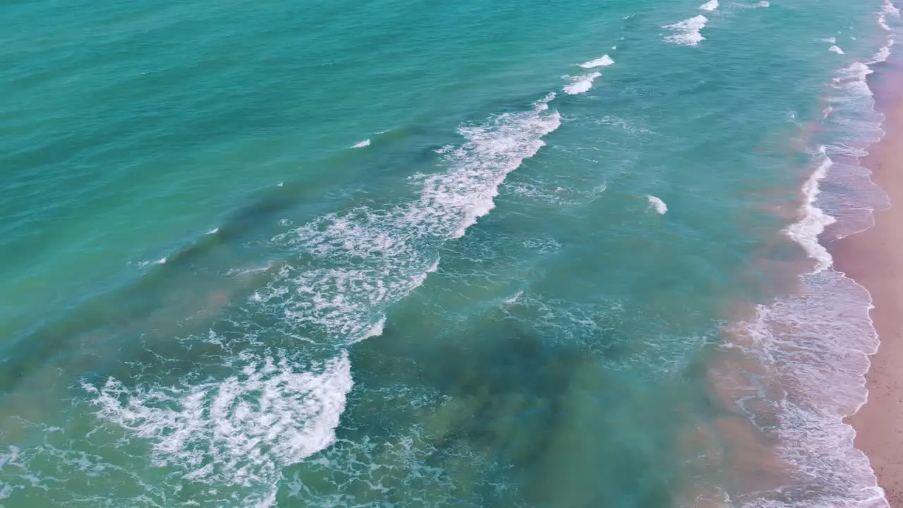 High drone aerial shot over waves breaking on a pink sand beach moving out to sea