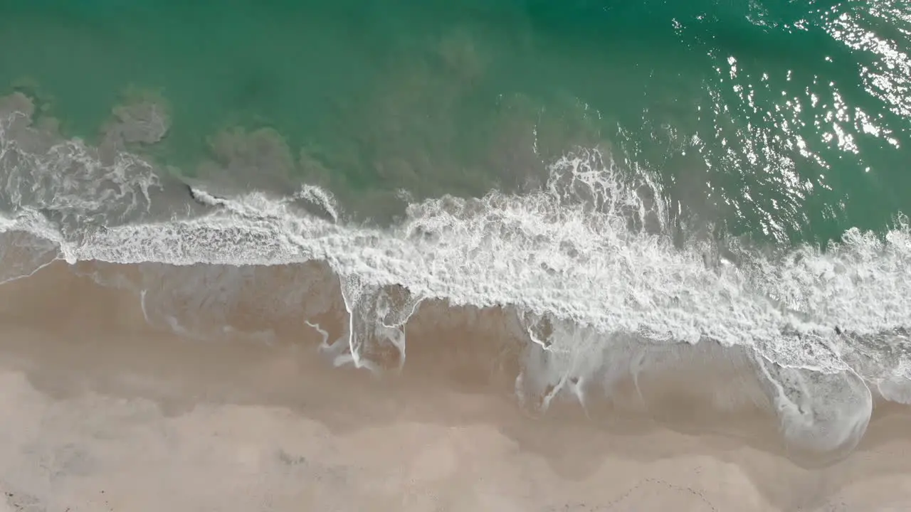 Slow aerial top down shot of crystal clear lagoon beach with crashing waves in Caribbean