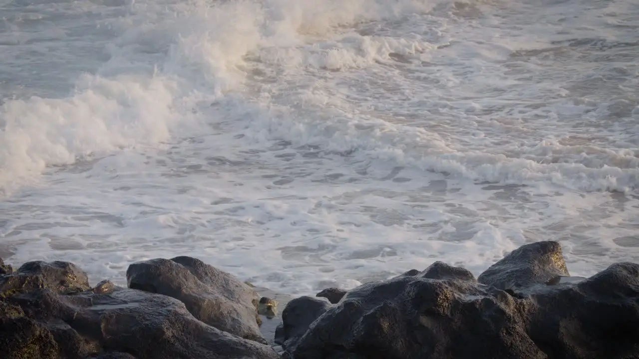 Blue waves roll into the coast of Hawaii in slow motion and break along a craggy coast 1