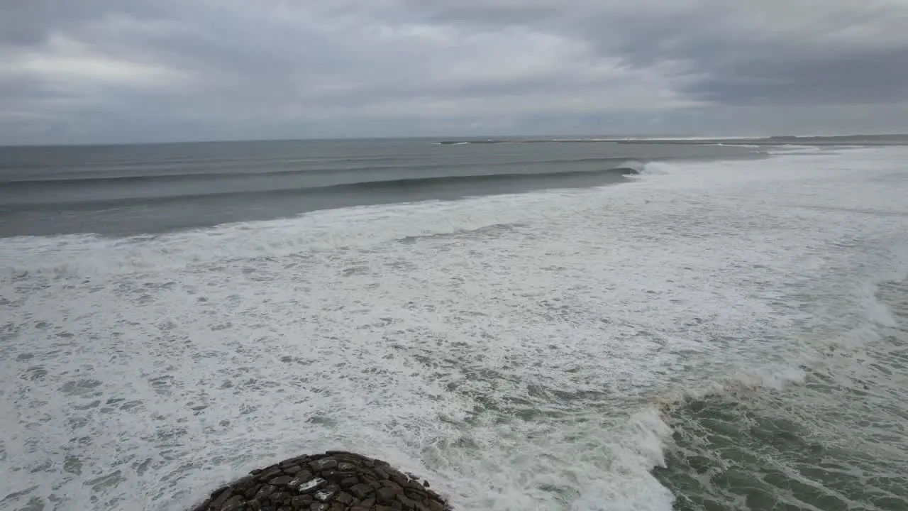 Aerial view of a rocky pier with sandy beach and oceans waves