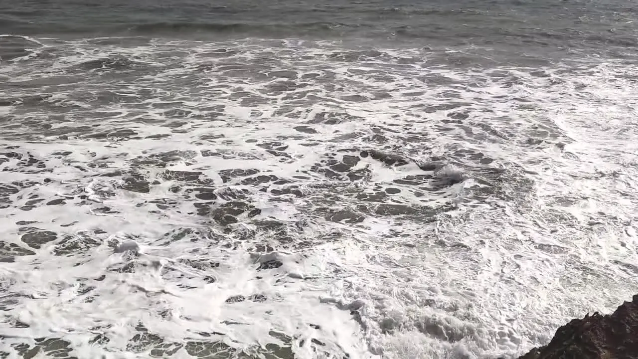 A panning shot of a beautiful sea where waves are crashing on the boulders by the sea