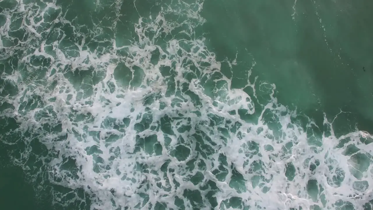 A rising aerial perspective looking straight down at the ocean with waves rolling in