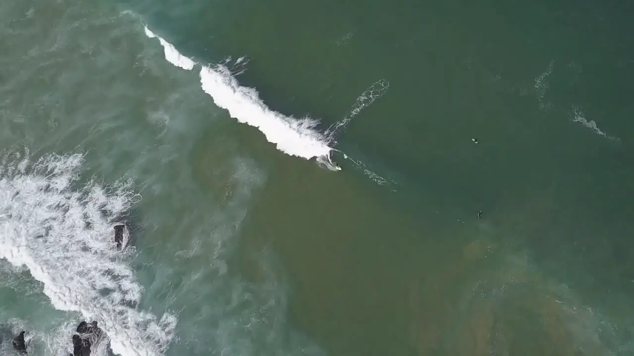 A drone rotates around an aerial view of surfers surfing and waves crashing