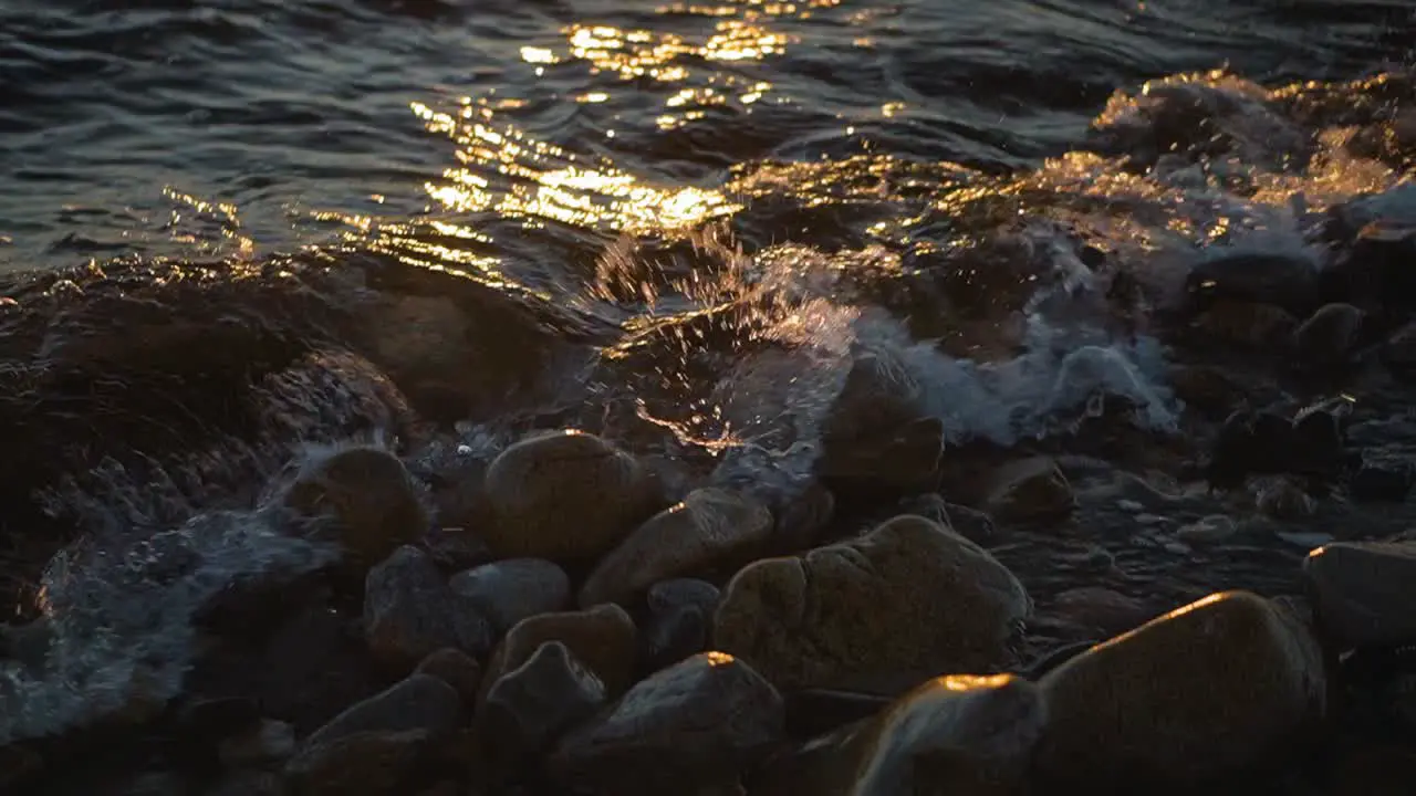 Ocean water waves crashing on a rocky shoreline at sunset on rocks on the coastline