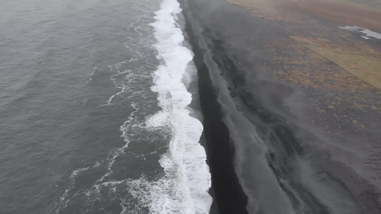 Tilt up aerial of black lava beach and waves of the sea in Iceland