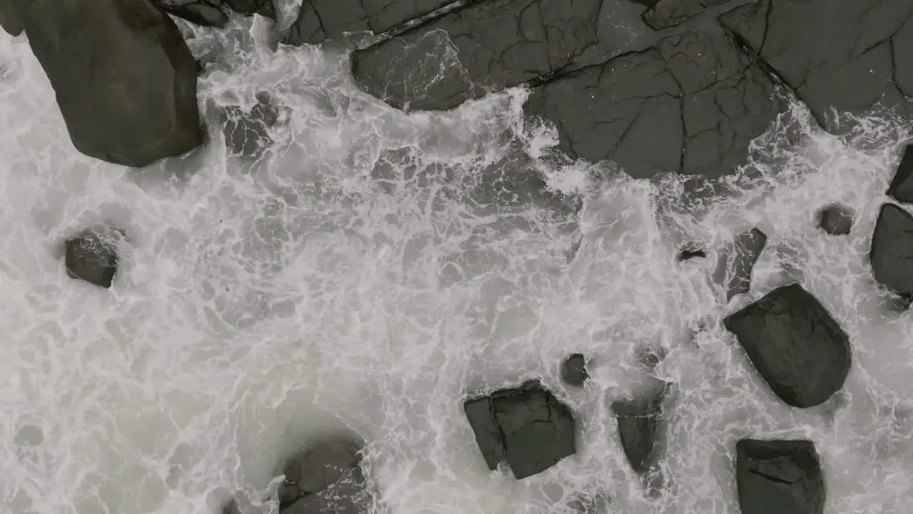 Close slow motion aerial footage top down of ocean waves crashing into rocks