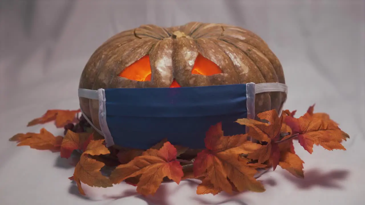 Halloween pumpkin with a face mask and autumn leaves