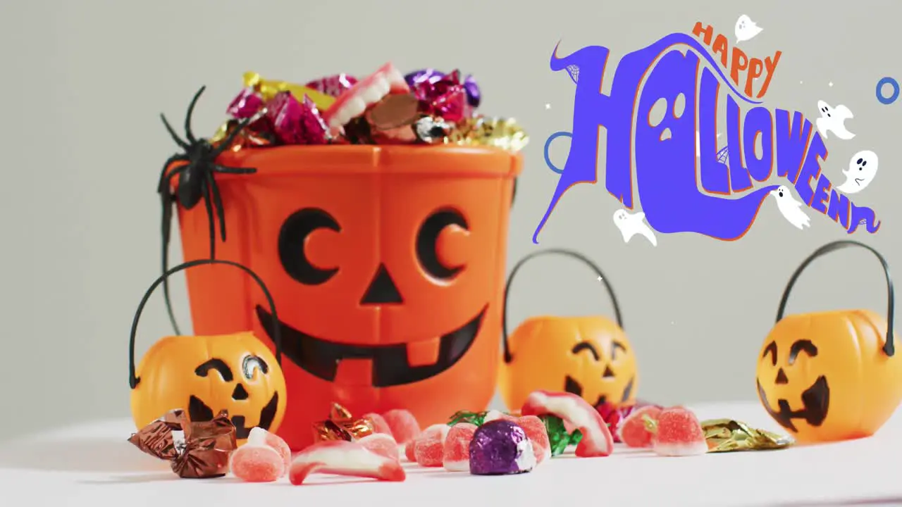 Happy halloween text banner and ghosts icons against pumpkin shaped bucket full of halloween candies