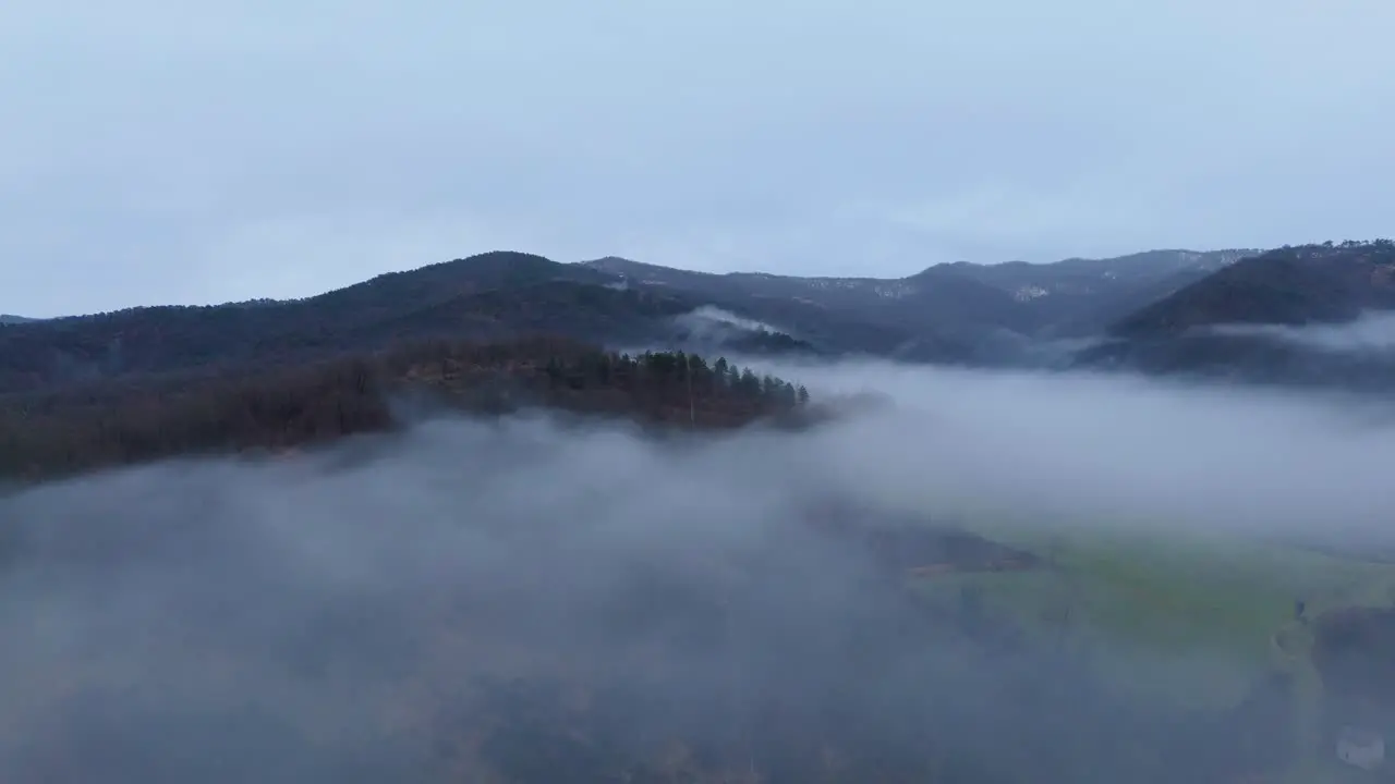 Cloud of mist hovering above hilly countryside below overcast sky