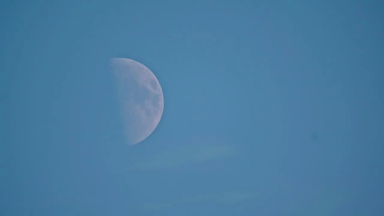 A Still Low Angle Shot Of The First Quarter Moon Moving Smoothly In The Clear Blue Sky