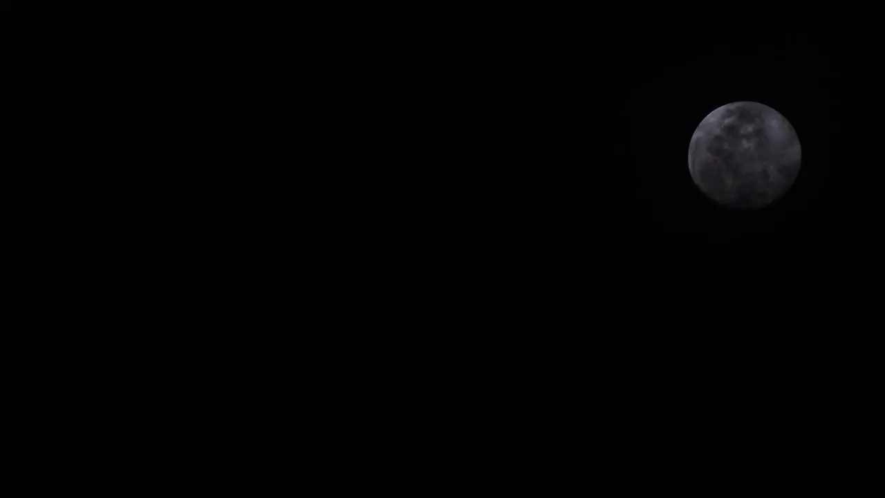 Telephoto Shot of Moon rising with a dark background and clouds in front of the moon