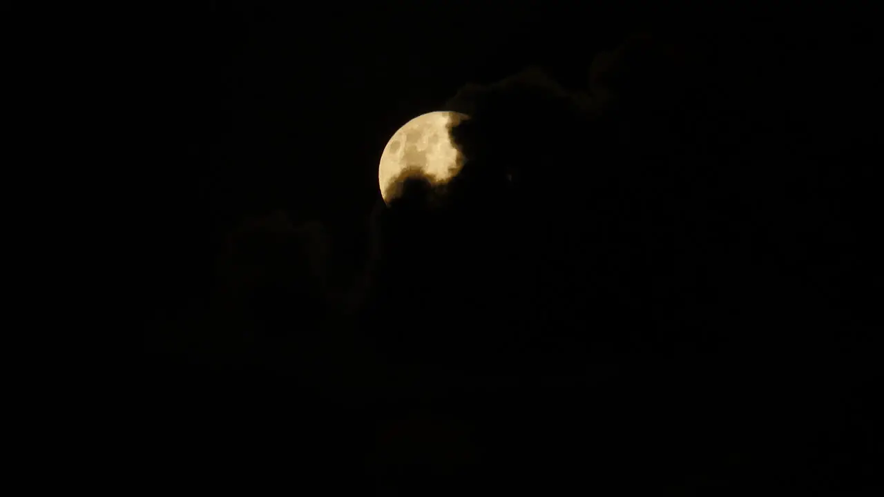 Black clouds slowly blow away revealing light yellow full moon in night sky